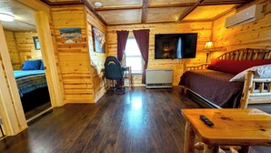 L'intérieur d'une cabane en bois, avec un lit, un bureau, une chaise et un téléviseur.
