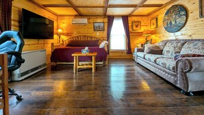 L’intérieur d’un chalet en bois, avec un lit, un canapé, un téléviseur et une table.