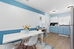 A modern kitchen with blue cabinets, a white countertop, and a dining area with a white table and chairs.