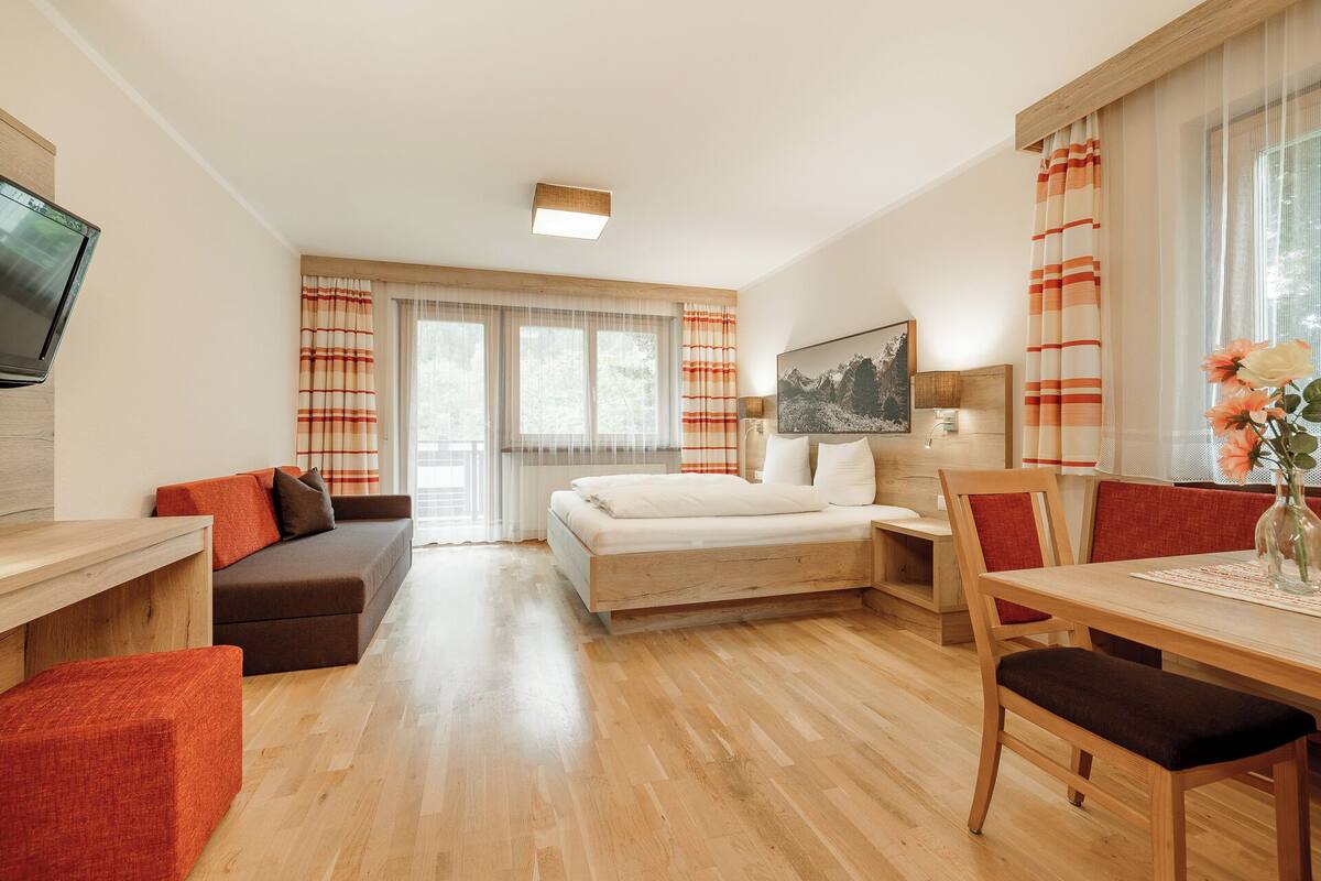 A hotel room with a bed, a desk, a sofa, and a dining table.