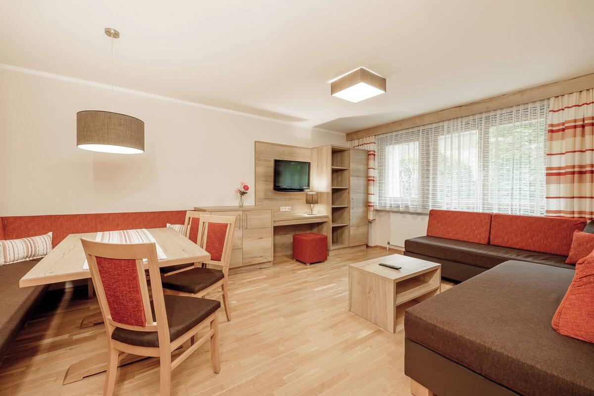 A modern living room with a wooden dining table, chairs, a sofa, and a TV.