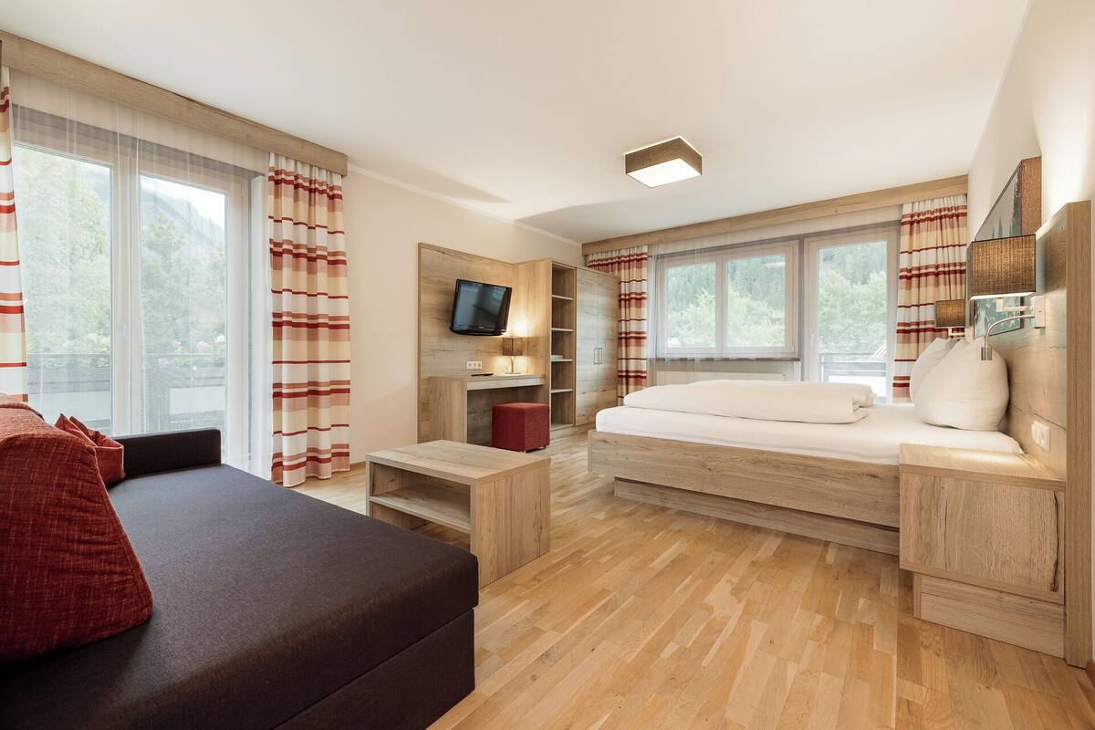 A modern bedroom with a bed, a TV, a desk, and a sofa.