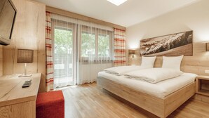 A modern hotel room with a wooden bed, a desk with a lamp, a red chair, and a large window with curtains.
