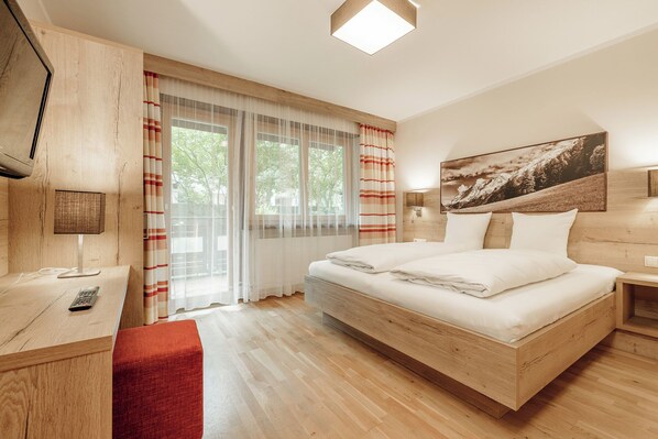 A modern hotel room with a wooden bed, a desk with a lamp, a red chair, and a large window with curtains. - MYALPS Pure (Oetz)