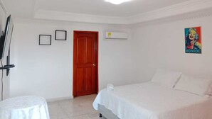 A bedroom with a bed, a small table, a door, and a poster on the wall. - Shalom Home90 Bella Habitacion, Cerca a Centros Comerciales (Barranquilla)
