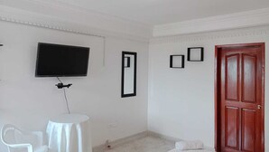 A room with a flat-screen TV mounted on the wall, a small round table with a chair, a wooden door, and a mirror. - Shalom Home90 Bella Habitacion, Cerca a Centros Comerciales (Barranquilla)