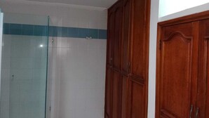 A bathroom with a glass shower enclosure, wooden cabinets, and a tiled wall with a blue stripe. - Shalom Home90 Bella Habitacion, Cerca a Centros Comerciales (Barranquilla)