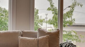 Un sofá beige con un plaid y almohadones en una habitación con ventanas grandes.