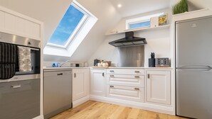 A modern kitchen with white cabinetry, a skylight, stainless steel appliances, and a wooden floor. - Picturesque cottage with views (Warmfield)