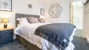 A bedroom with a bed, bedside table, lamp, wall art, and a TV. - Picturesque cottage with views (Warmfield)