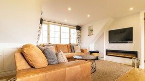 A modern living room with a leather sofa, a flat-screen TV, and a fireplace. - Picturesque cottage with views (Warmfield)