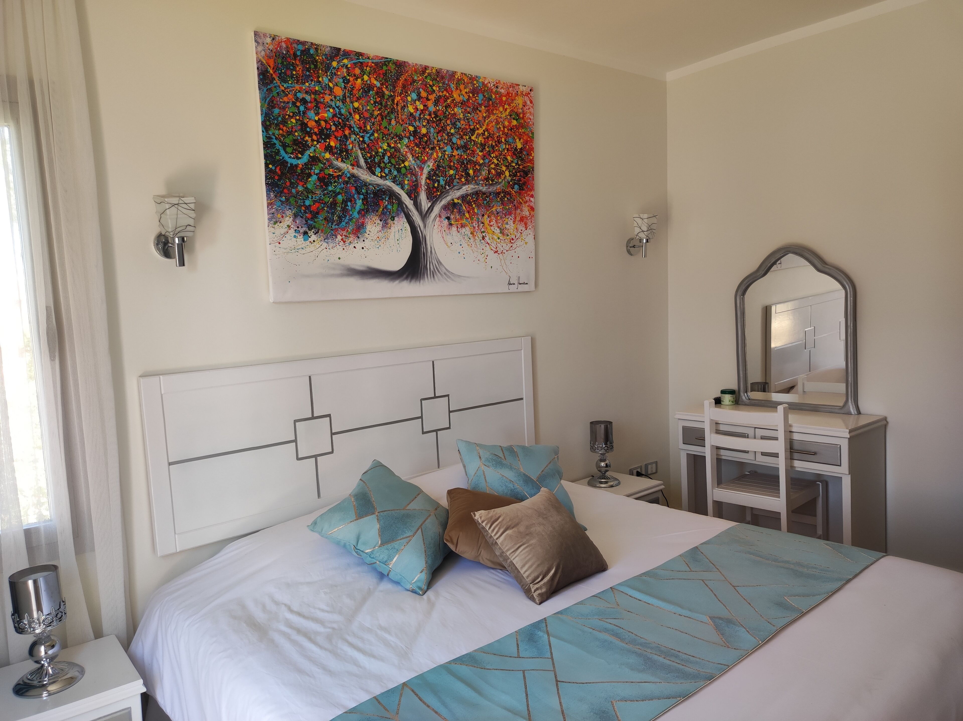 A neatly arranged bedroom with a bed, bedside tables, a dresser, and a large abstract painting on the wall.