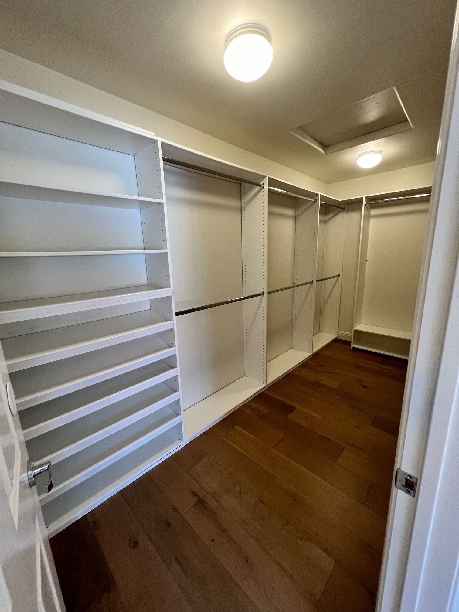 Un vestidor con estantes abiertos y puertas cerradas, suelo de madera y una lámpara en el techo.