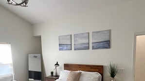 Une chambre à coucher comprenant un lit, des tables de chevet, une commode, un miroir, une fenêtre et un lustre.