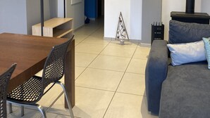 A modern living room with a wooden dining table, a black metal chair, a grey sofa with a blue cushion, a small decorative tree, and a black fireplace. - Appartement Les Orres Chef Lieu (Les Orres Chef Lieu)