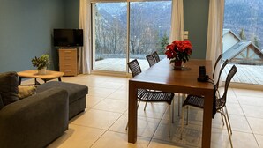 A modern living room with a dining area, a flat-screen TV, and a large window with a view of a snowy landscape. - Appartement Les Orres Chef Lieu (Les Orres Chef Lieu)