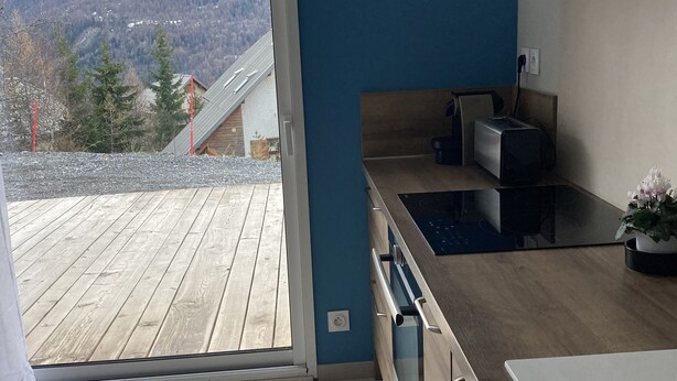 A modern kitchen with a large window, a wooden deck, and a view of a mountainous landscape. - Appartement Les Orres Chef Lieu (Les Orres Chef Lieu)