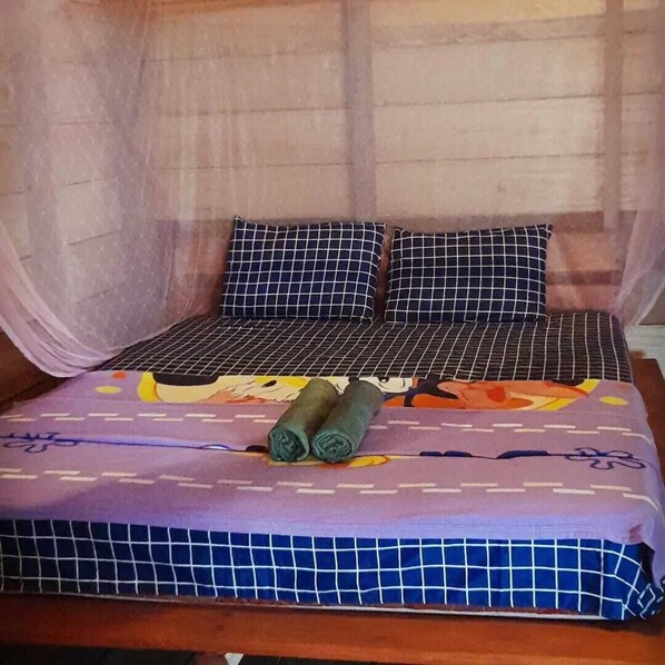 Una cama con una colcha morada, dos almohadas con estampado a cuadros y una toalla enrollada.