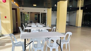 Un vaste espace intérieur doté de nombreuses tables et chaises blanches, d’un plafond haut et d’un escalier menant à un niveau supérieur.