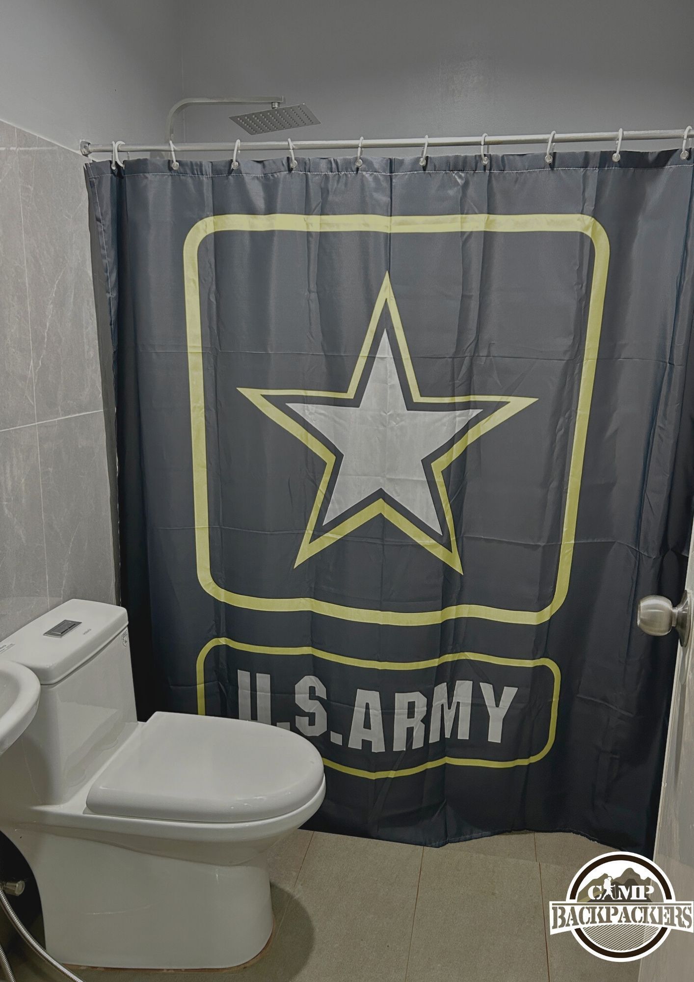 A bathroom with a shower curtain featuring a star and 'U.S. ARMY' text, a white toilet, and a showerhead.