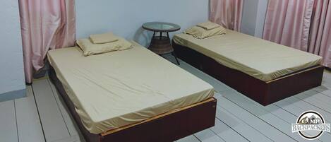 Una habitación con dos camas, una mesita redonda y cortinas rosadas.