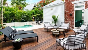 A wooden deck with lounge chairs and a small pool, surrounded by lush greenery and a brick building. - Grand Maloney Hotel (Key West)