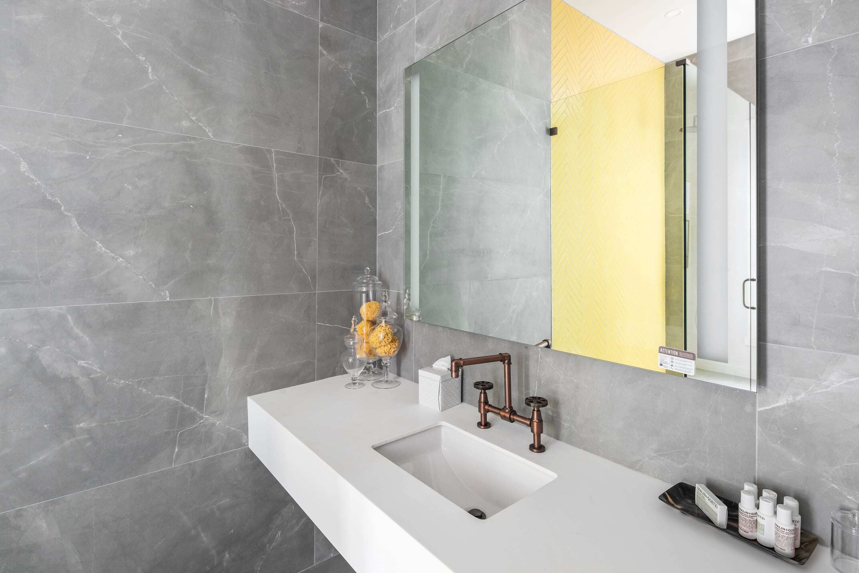 A modern bathroom with a white sink, copper faucet, and a large mirror.