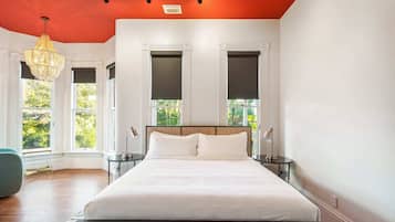 Une chambre à coucher avec un grand lit, deux tables de chevet, un luminaire suspendu et des fenêtres équipées de stores.