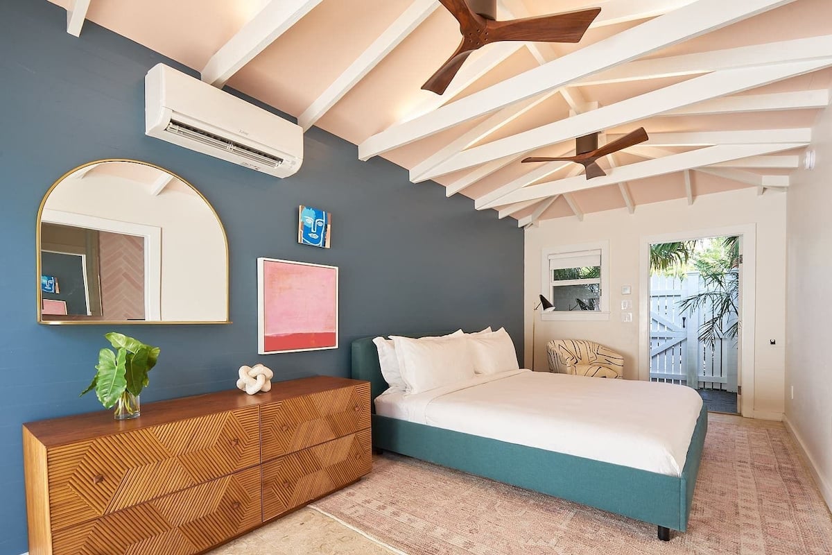 A bedroom with a bed, a dresser, a mirror, and an air conditioning unit.