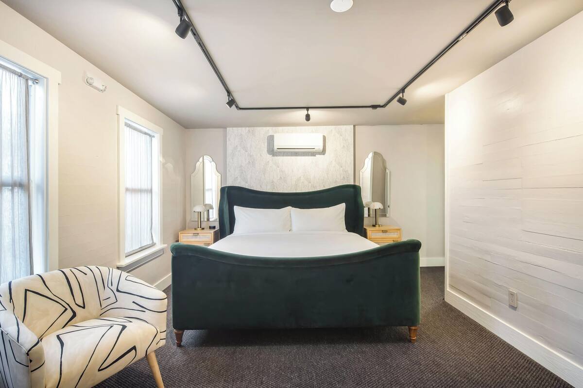 A neatly arranged bedroom with a large bed, a chair, and a wall-mounted air conditioner.