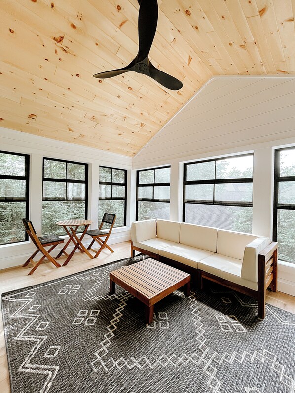Une pièce spacieuse avec un plafond haut, de grandes fenêtres, un canapé, une table basse et un ventilateur de plafond.