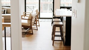 Ein geräumiges Zimmer mit einer großen Schiebetür und Zugang zu einem Balkon, einem Essbereich mit Holzkästen und Tisch sowie einer Küchenzeile mit Kühlschrank und Spüle.