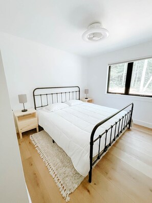 Ein Schlafzimmer mit einem Bett, einem Nachttisch, einer Lampe, einem Fenster und einer Deckenleuchte.