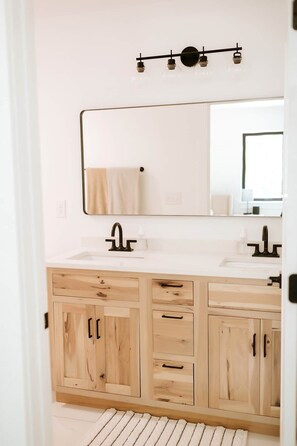 Ein Badezimmer mit weißer Ablage, zwei Waschbecken, einem Spiegel und Holzschränken.