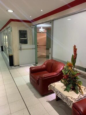 Een hotel lobby met een rode leren bank, een tafel met een kant kleedje, en een bord dat een restaurant aangeeft.
