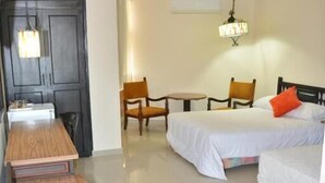 Une chambre d’hôtel avec deux lits, un bureau en bois, une poubelle et une petite table avec des chaises.