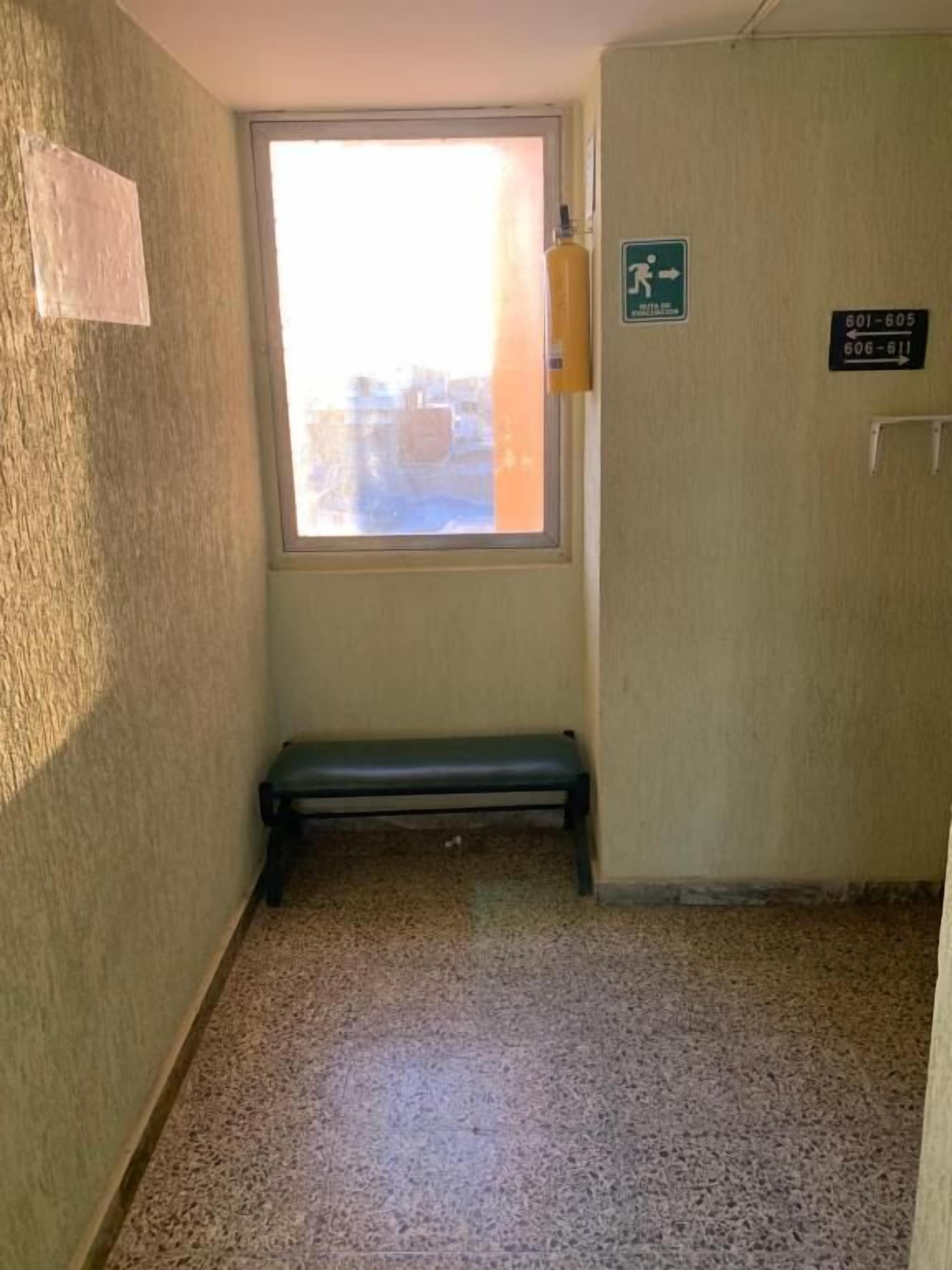 A small room with a bench, a window, and a door with emergency exit signs.