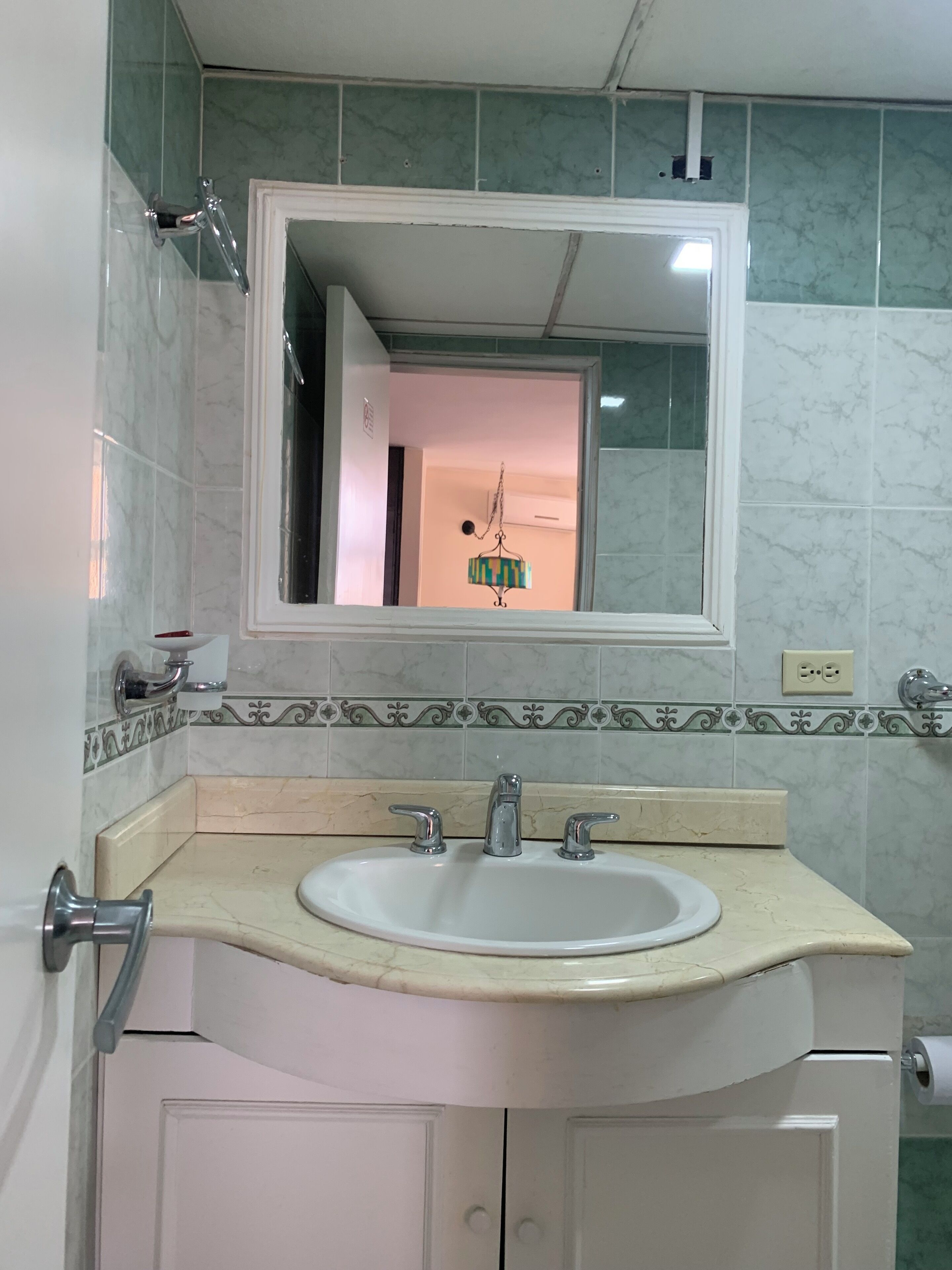 A bathroom with a white sink, two faucets, a mirror above the sink, and a toilet with a white seat.