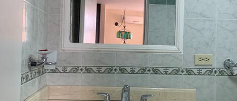 A bathroom with a white sink, two faucets, a mirror above the sink, and a toilet with a white seat.