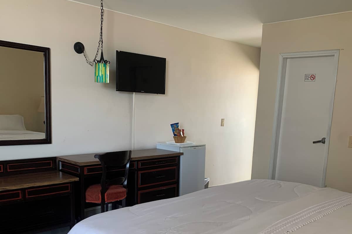 Ett hotellrum med en stor säng, ett skrivbord med en stol, en tv som är monterad på väggen och en dörr med en skylt.