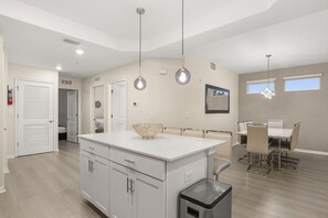 Una cocina moderna con una isla central, iluminación colgante y un comedor con mesa y sillas.