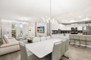 Una cocina moderna con armarios blancos, una isla central y un comedor con mesa y sillas blancas.