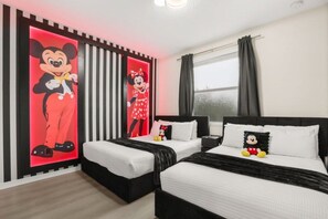A hotel room with two beds, a large Mickey Mouse and Minnie Mouse poster on the wall, and a window with curtains.