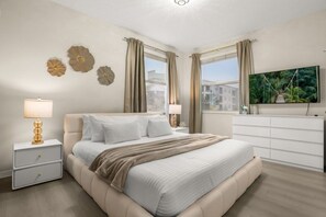 Un dormitorio con cama, mesitas de noche, televisor y cortinas.