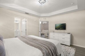 Ein Schlafzimmer mit Bett, Kommode, Fernseher und einer Tür zu einem Badezimmer.