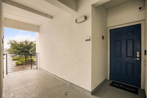 Un couloir avec une porte bleue, un paillasson et une vue sur la verdure à l’extérieur.