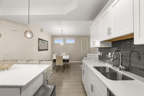 Una cocina moderna con muebles blancos, una isla grande con fregadero y un comedor con mesa y sillas.