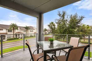 A balcony with a table and chairs, a potted plant, and a view of residential buildings and greenery.