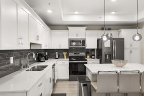 Une cuisine moderne avec des meubles blancs, une cuisinière noire, un four à micro-ondes et un réfrigérateur. On y trouve également des luminaires suspendus et une table à manger avec des chaises.
