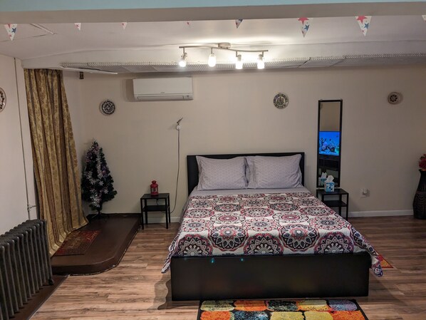 Une chambre à coucher avec un lit, une petite table, un radiateur, un sapin de Noël et un climatiseur fixé au mur.